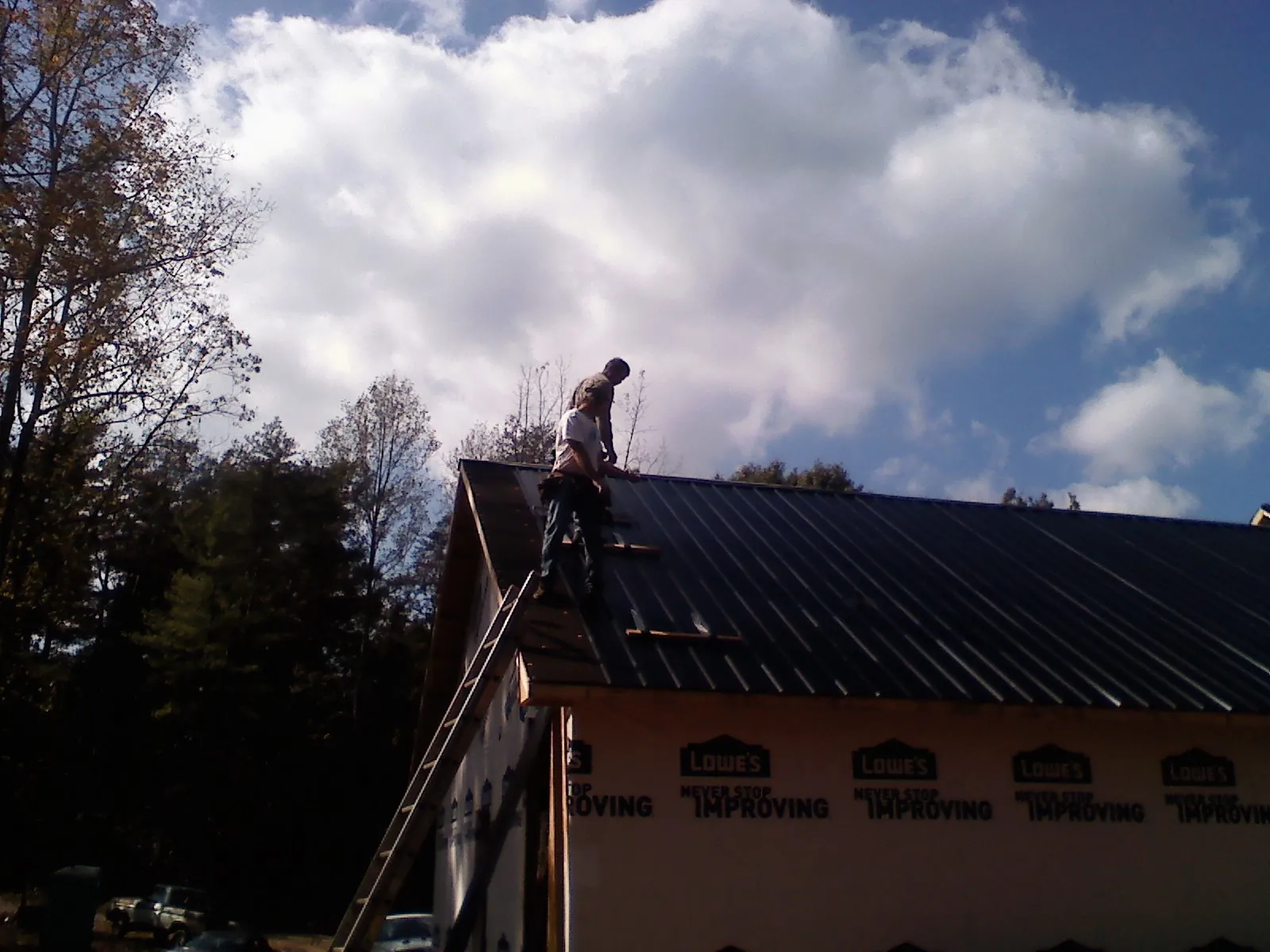 Roofer fastening dark metal panels high against a cloudy sky, from a Roof Inspection job in Converse